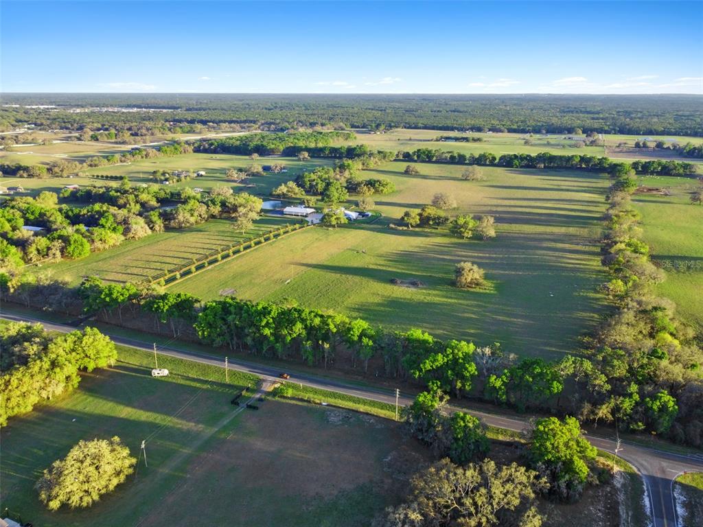 An aerial view shows a large, grassy pasture with scattered trees and a paved road — 0 W CR 476, BUSHNELL, FL