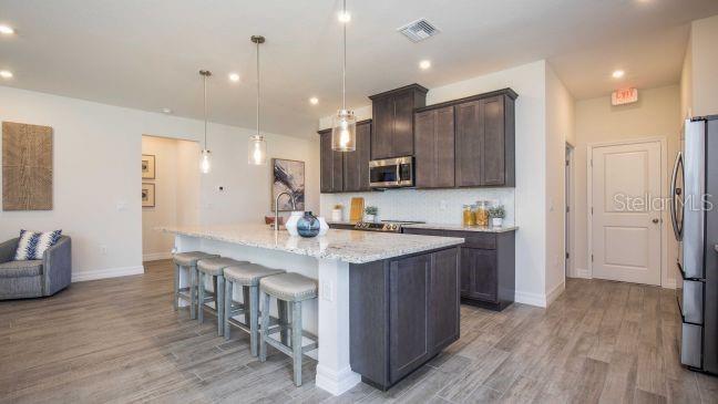 A modern kitchen features dark wood cabinets, granite countertops, a large island, and wood-look flooring — 17641 NW 168TH ROAD, ALACHUA, FL