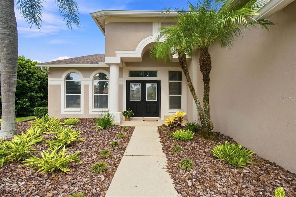 A concrete walkway leads to the front entrance of a beige house with double doors — 10260 SHADOW BRANCH DRIVE, TAMPA, FL
