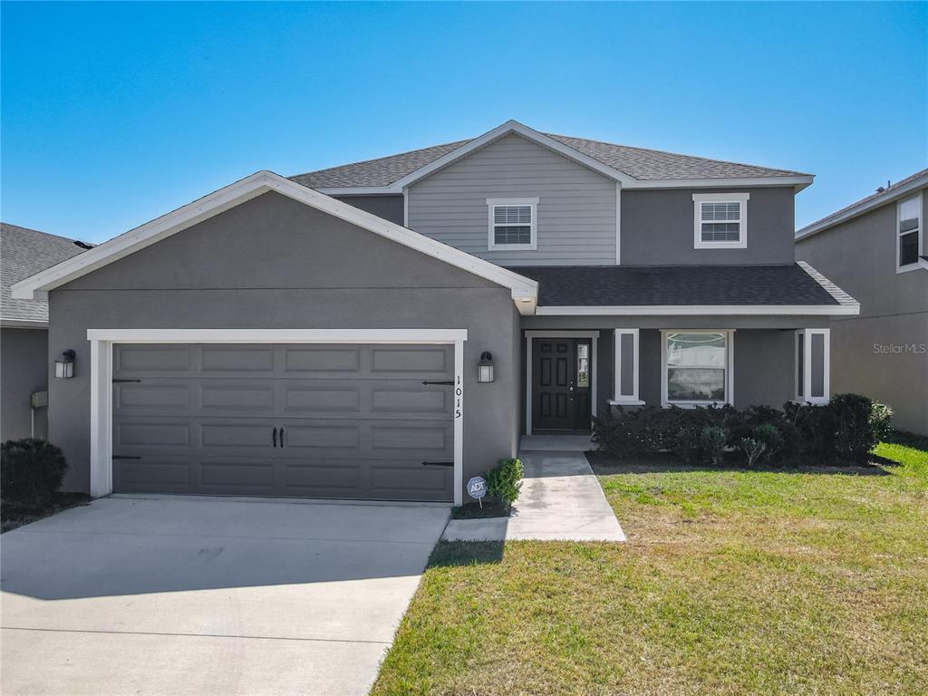 A two-story gray house features a two-car garage, a front walkway, and a dark door — 1015 CORSO DRIVE, WINTER HAVEN, FL