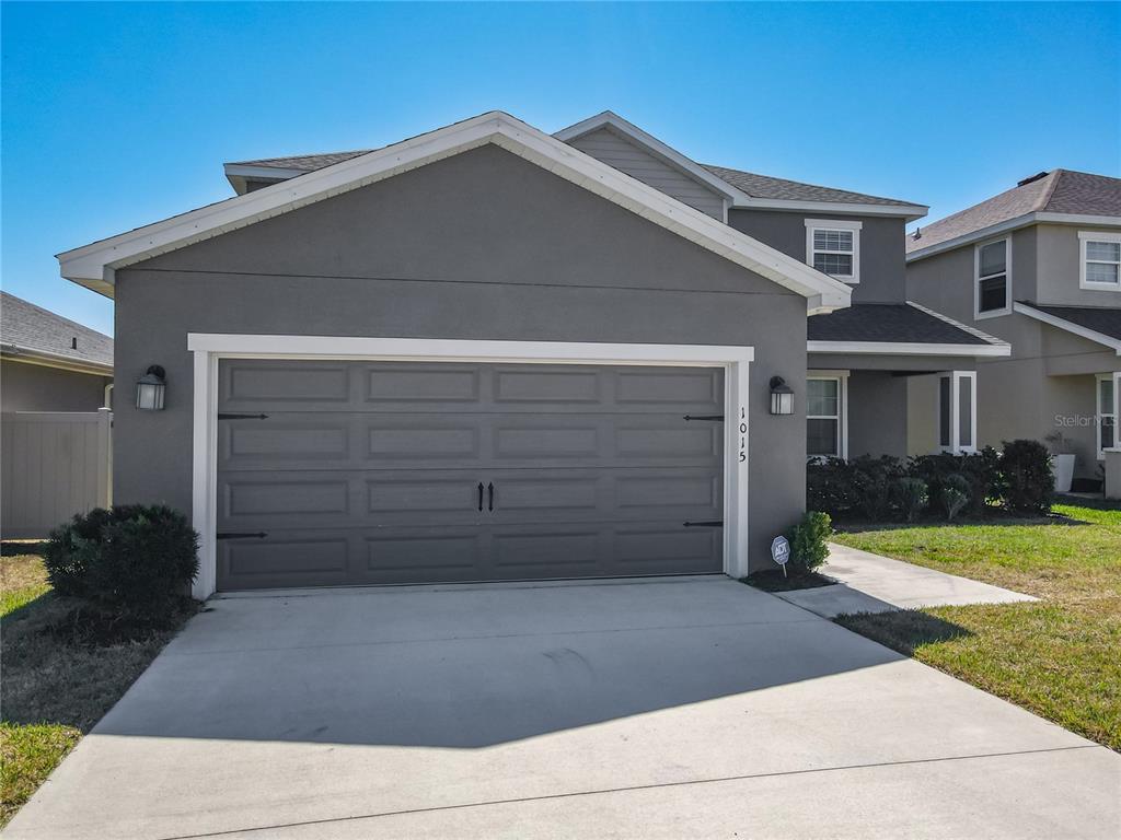 A two-story house features a gray stucco exterior, a two-car garage, and a concrete driveway — 1015 CORSO DRIVE, WINTER HAVEN, FL