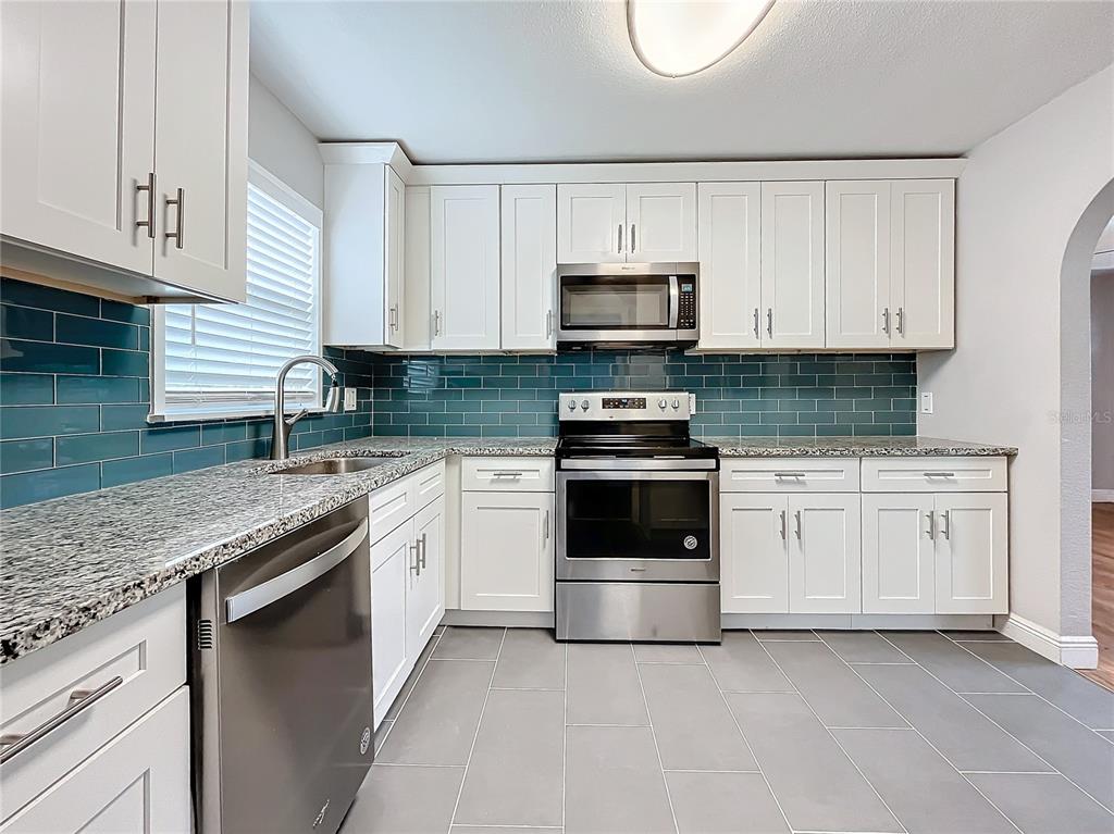 A kitchen features white cabinets, stainless steel appliances, granite countertops, and a teal backsplash — 5340 5TH AVENUE S, ST PETERSBURG, FL