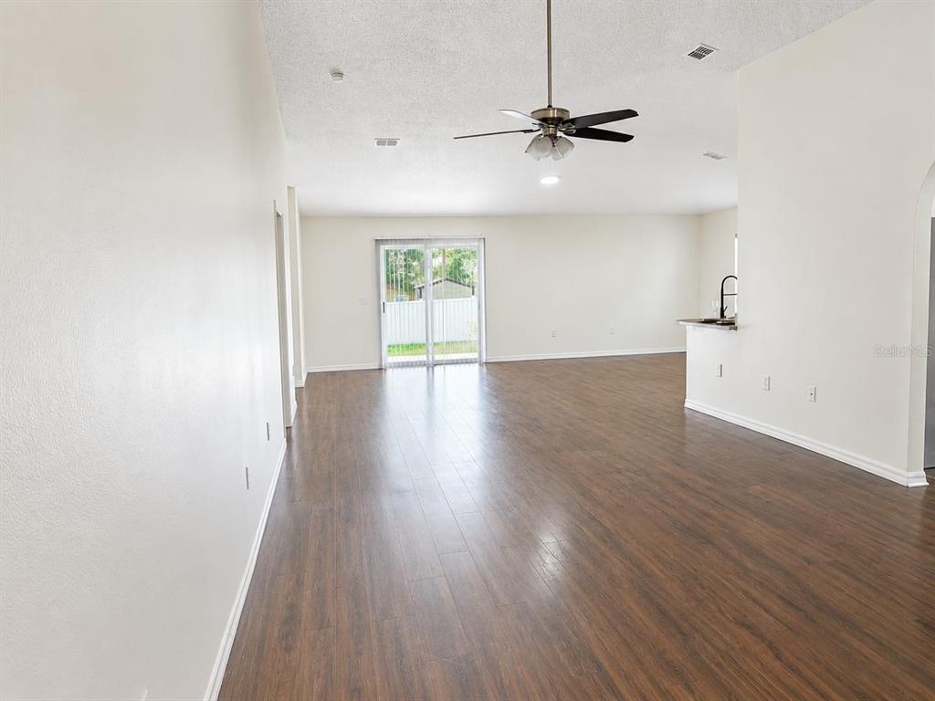 An open-concept living area features wood-look flooring, a ceiling fan, and sliding glass doors — 13402 COPPER HEAD DRIVE, RIVERVIEW, FL