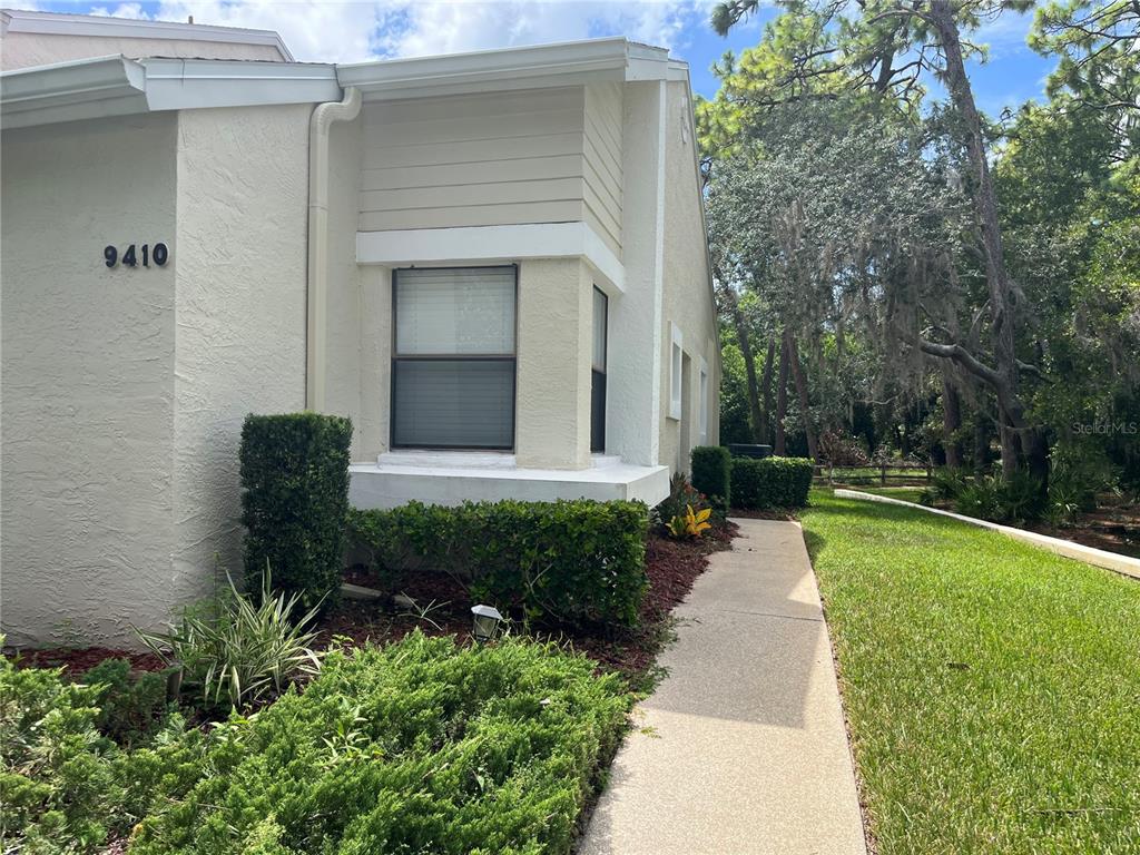 A beige stucco building exterior with a walkway, landscaping, and a window under a roofline — 9410 NAKOMA WAY UNIT H, WEEKI WACHEE, FL