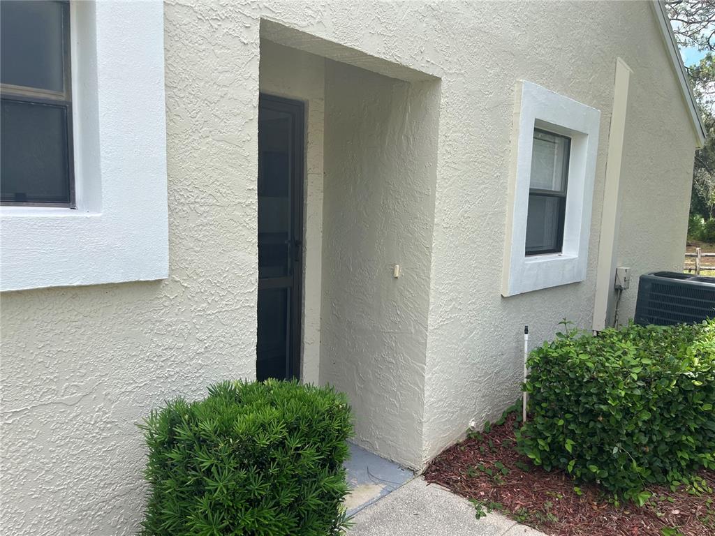 A beige stucco exterior features a recessed front entryway flanked by two windows and landscaping — 9410 NAKOMA WAY UNIT H, WEEKI WACHEE, FL