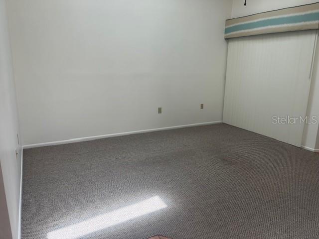 An empty room features beige carpeting, white walls, and vertical blinds over a sliding door — 9410 NAKOMA WAY UNIT H, WEEKI WACHEE, FL