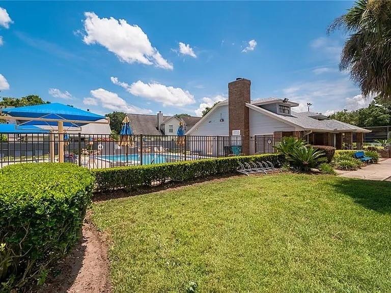 A grassy lawn leads to a community pool area with blue umbrellas and a clubhouse — 3161 BERRIDGE LANE, ORLANDO, FL