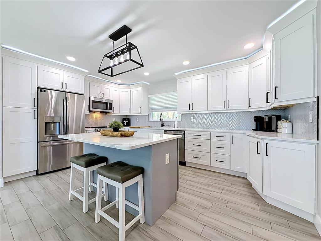 A modern kitchen features white cabinetry, a gray island with two stools, and herringbone backsplash — 1509 BARBARA AVENUE, CLEARWATER, FL