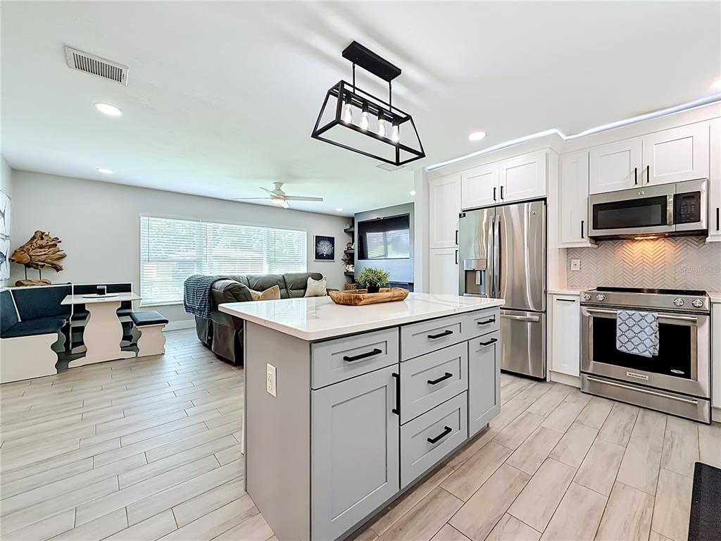 A kitchen with a light gray island, white cabinets, stainless steel appliances, and adjacent dining area — 1509 BARBARA AVENUE, CLEARWATER, FL