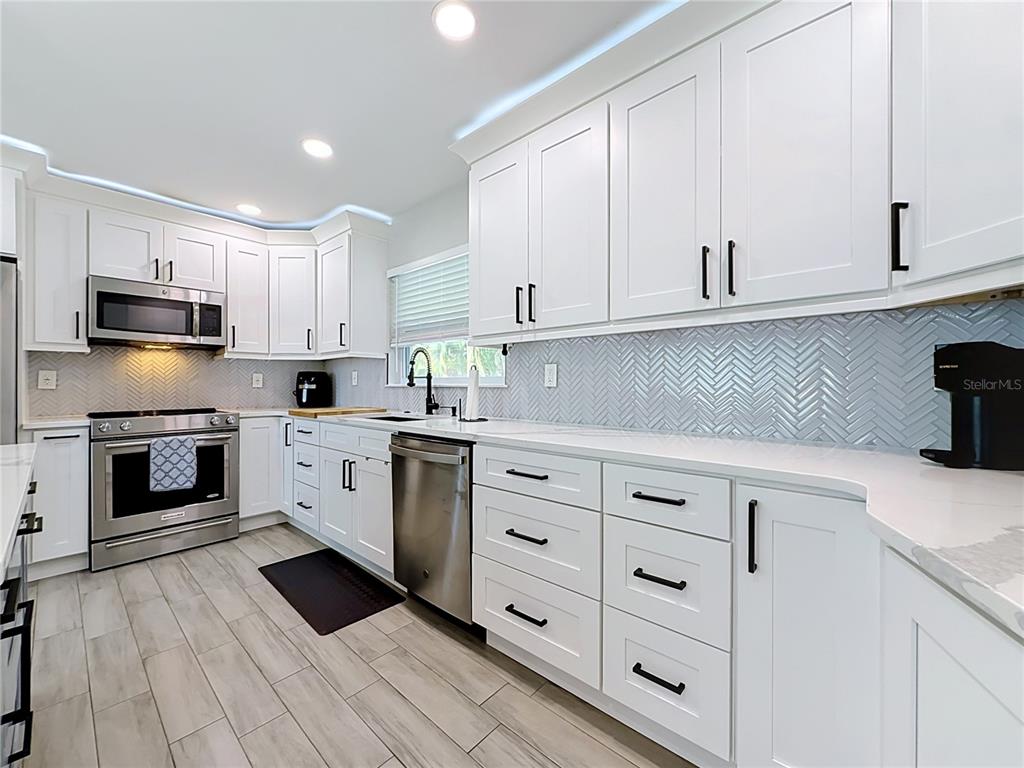A modern kitchen features white shaker cabinets, stainless steel appliances, and a light blue herringbone backsplash — 1509 BARBARA AVENUE, CLEARWATER, FL