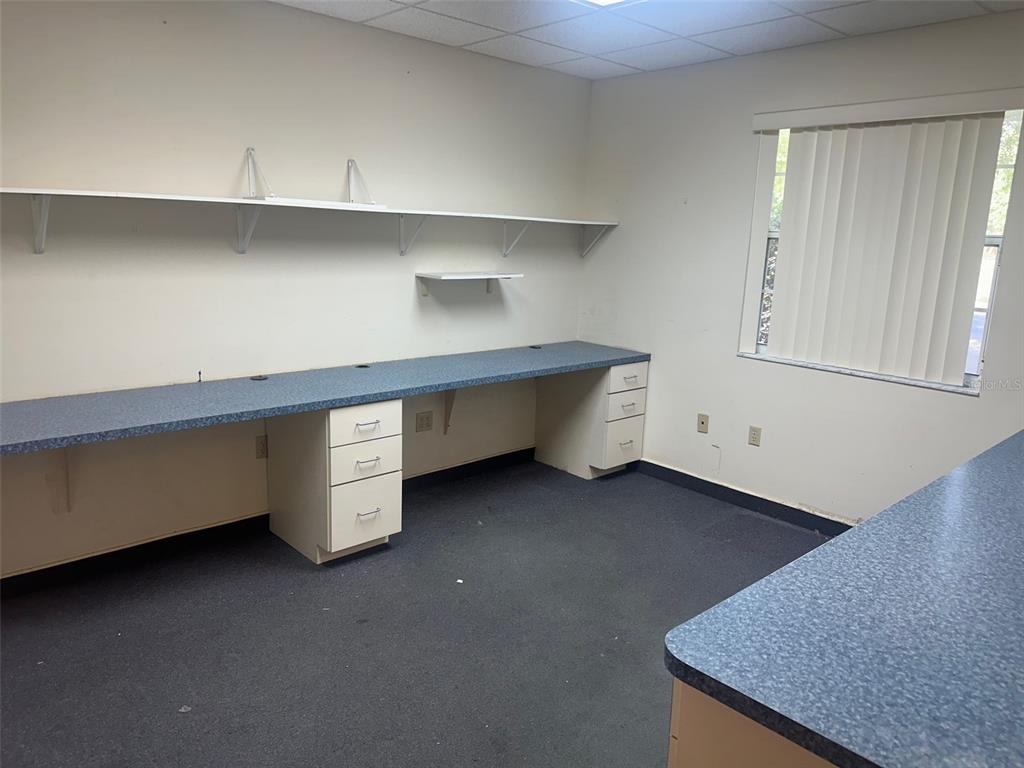 An office room features blue laminate countertops, white drawer units, wall-mounted shelving, and a window — 4611 NW 53RD AVENUE, GAINESVILLE, FL