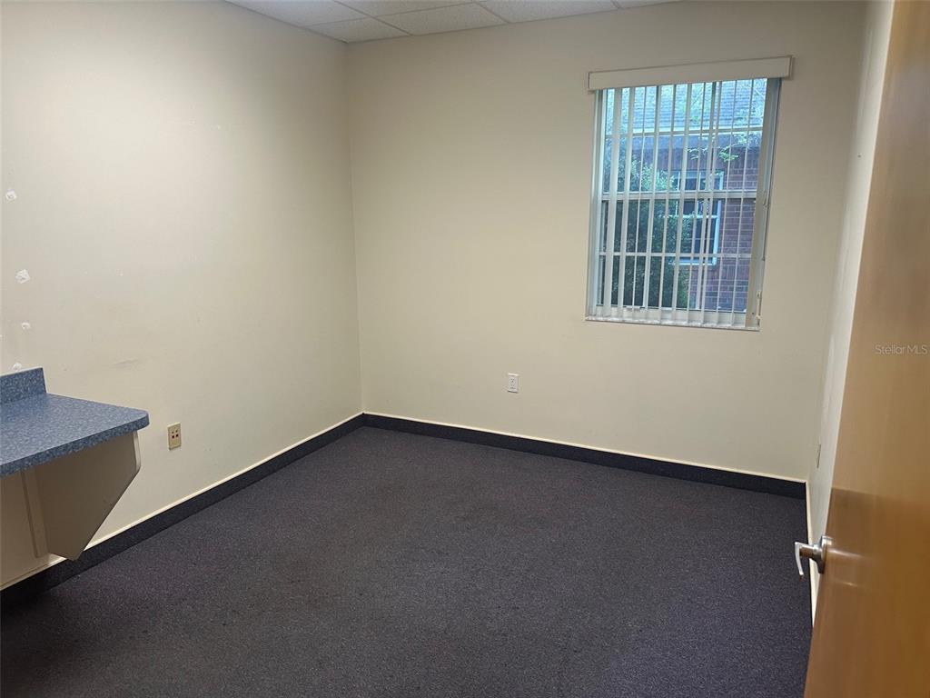 An empty office with beige walls, dark carpet, a blue countertop, and a window with blinds — 4611 NW 53RD AVENUE, GAINESVILLE, FL