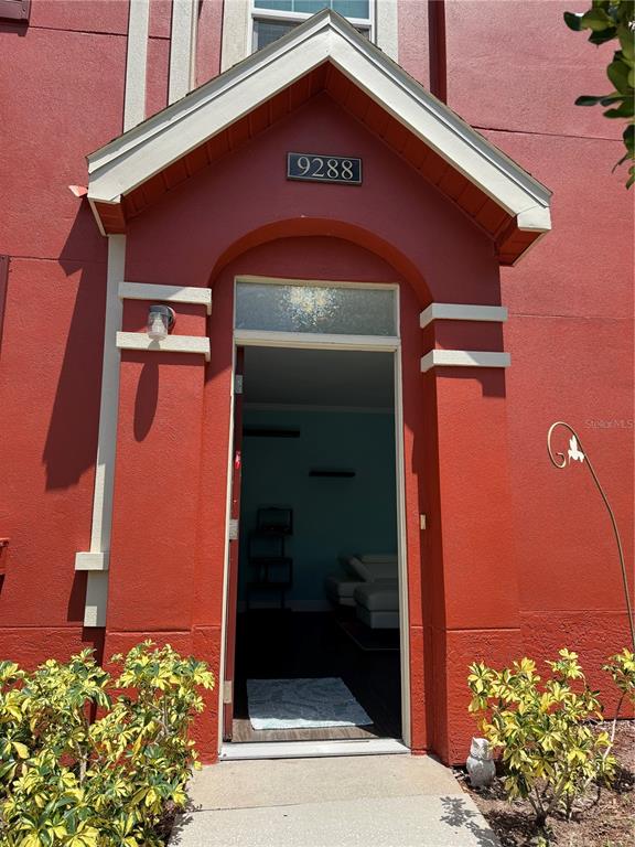 A red exterior entryway features a gabled roof, a house number, and an open doorway — 9288 LAKE CHASE ISLAND WAY, TAMPA, FL