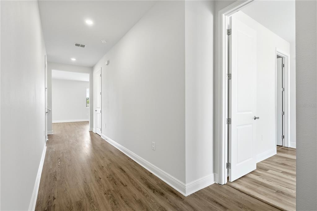 A hallway with light wood-look flooring leads to an open room with white walls — 1128 SUGARWOOD STREET, DAVENPORT, FL
