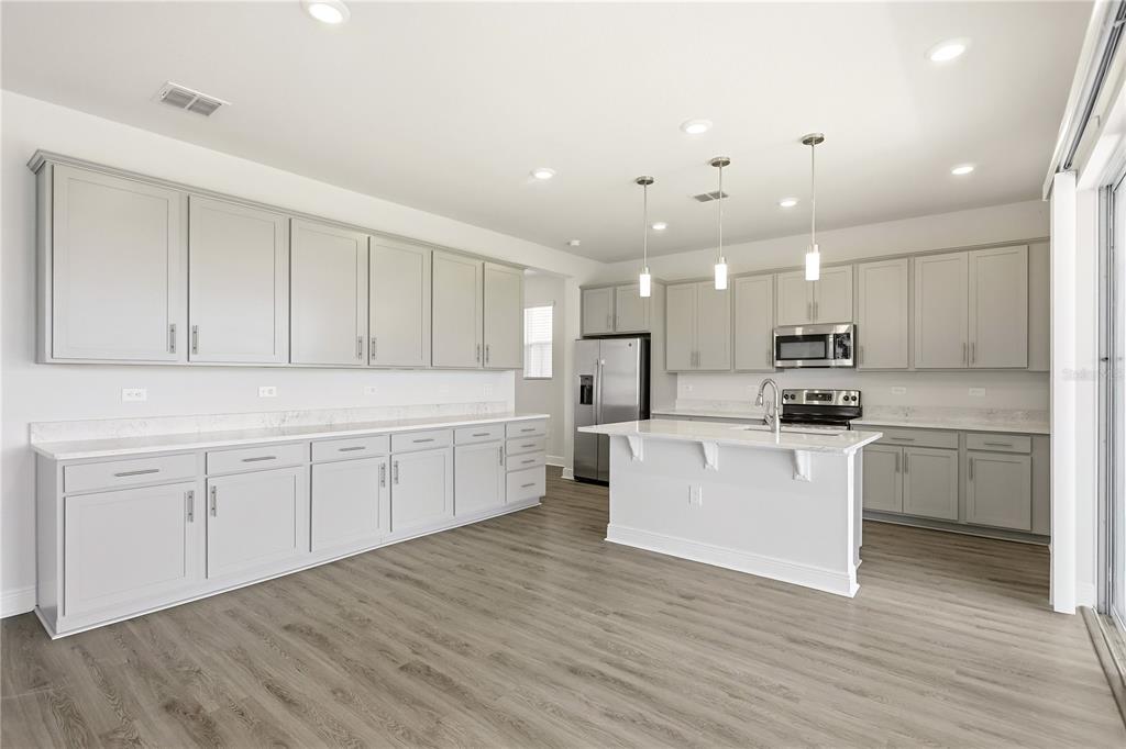 A modern kitchen features light gray cabinets, white countertops, stainless steel appliances, and wood-look flooring — 1128 SUGARWOOD STREET, DAVENPORT, FL