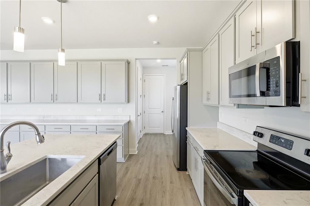 A modern kitchen features light gray cabinets, white countertops, stainless steel appliances, and a central island — 1128 SUGARWOOD STREET, DAVENPORT, FL
