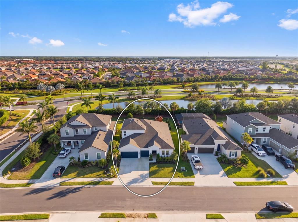 An aerial view shows a single-family house with a driveway and lawn facing a pond — 16552 STAR GRASS CIRCLE, BRADENTON, FL