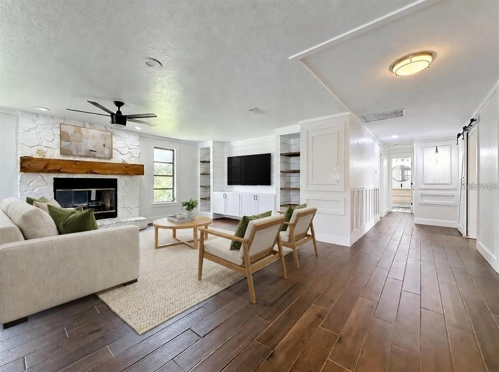 A living room features a white stone fireplace, wood flooring, and built-in shelving around a television — 12756 POINSETTIA AVENUE, SEMINOLE, FL