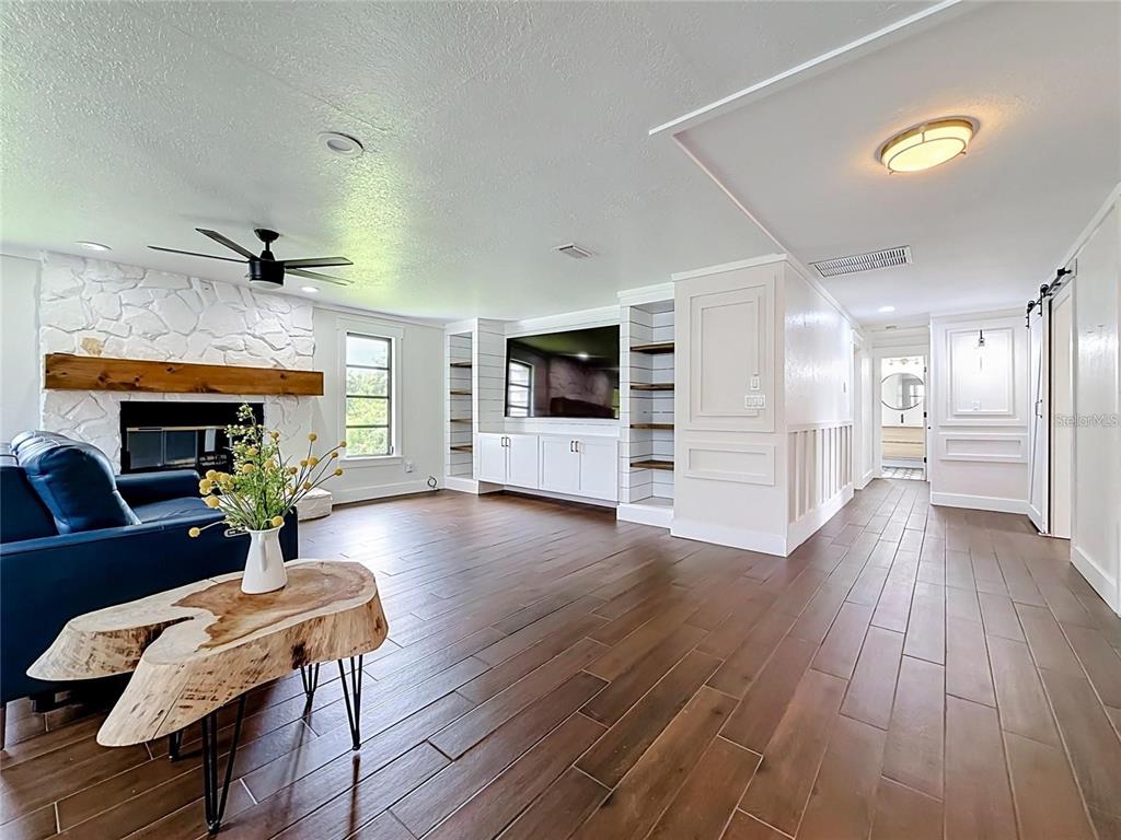 A living room features a stone fireplace, built-in shelving, a television, and wood-look tile flooring — 12756 POINSETTIA AVENUE, SEMINOLE, FL