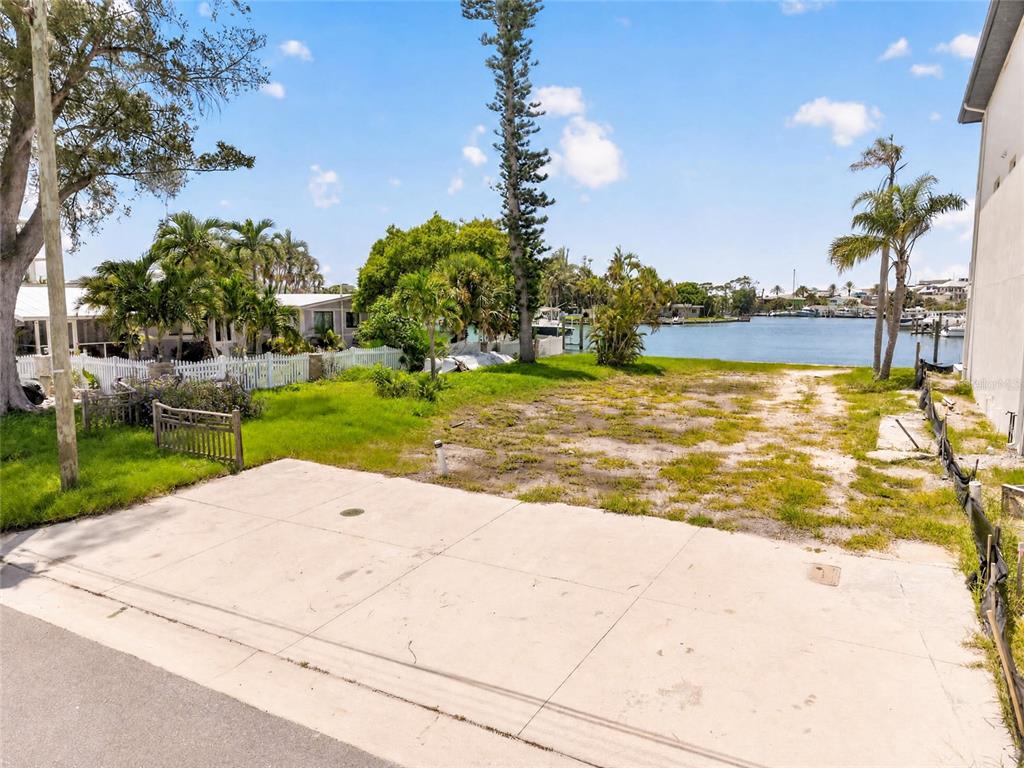 A vacant waterfront lot features a concrete driveway leading toward a canal with palm trees — 331 BOCA CIEGA DRIVE, MADEIRA BEACH, FL