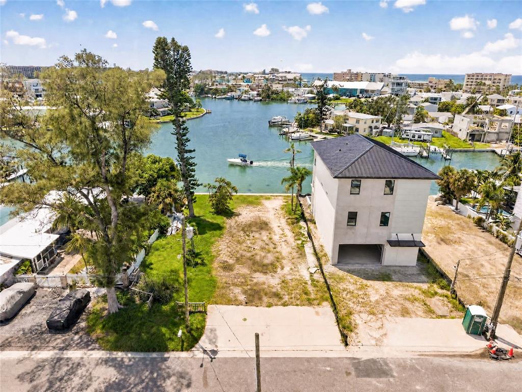An aerial view shows a vacant waterfront lot next to a modern three-story house — 331 BOCA CIEGA DRIVE, MADEIRA BEACH, FL