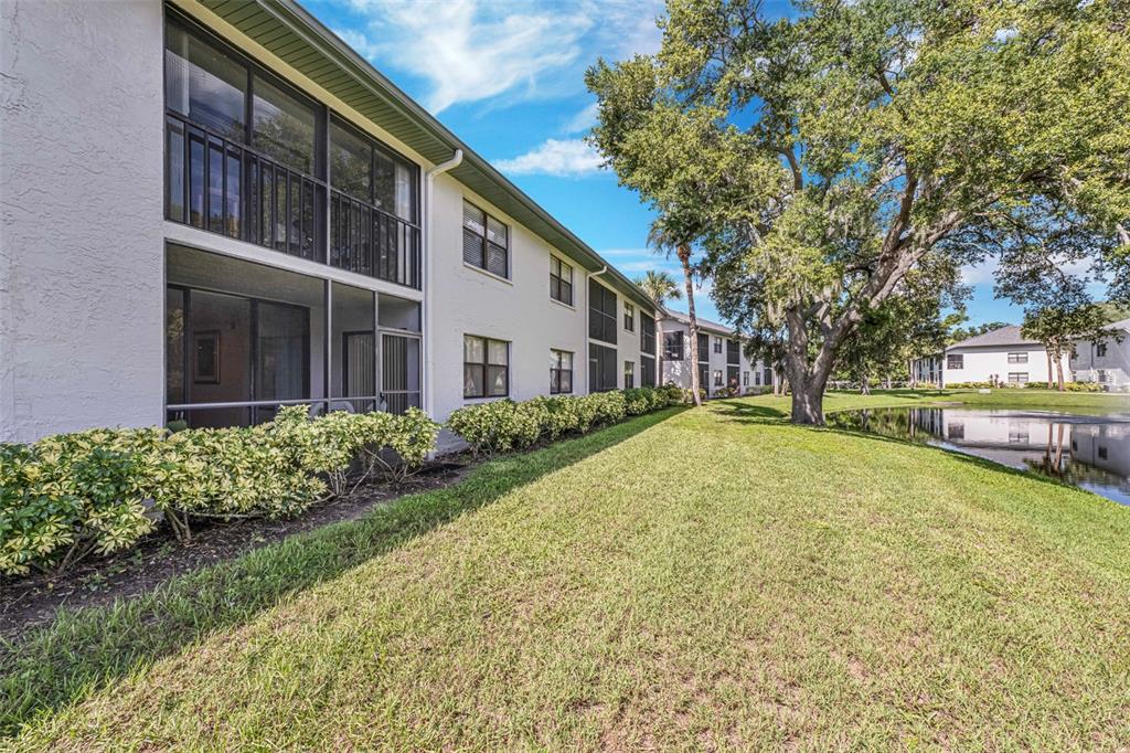 A multi-story apartment building with screened balconies overlooks a grassy lawn and a small pond — 4520 47TH AVENUE W UNIT 103, BRADENTON, FL