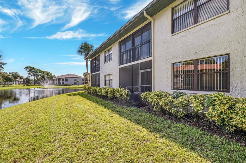 A two-story apartment building exterior with screened-in balconies, landscaping, and a pond with a fountain — 4520 47TH AVENUE W UNIT 103, BRADENTON, FL