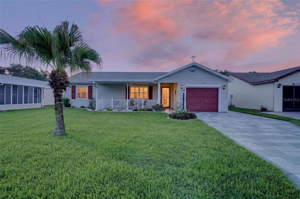 A single-story house with light siding, a red garage door, and a palm tree out front — 1218 SANTOS PLACE, THE VILLAGES, FL