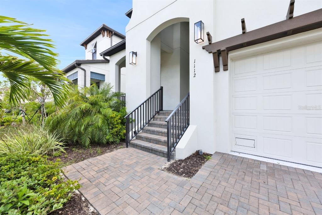 A white house exterior features a brick paver walkway, stairs with black railings, and garage — 1112 SEAGRAPE DRIVE, RUSKIN, FL