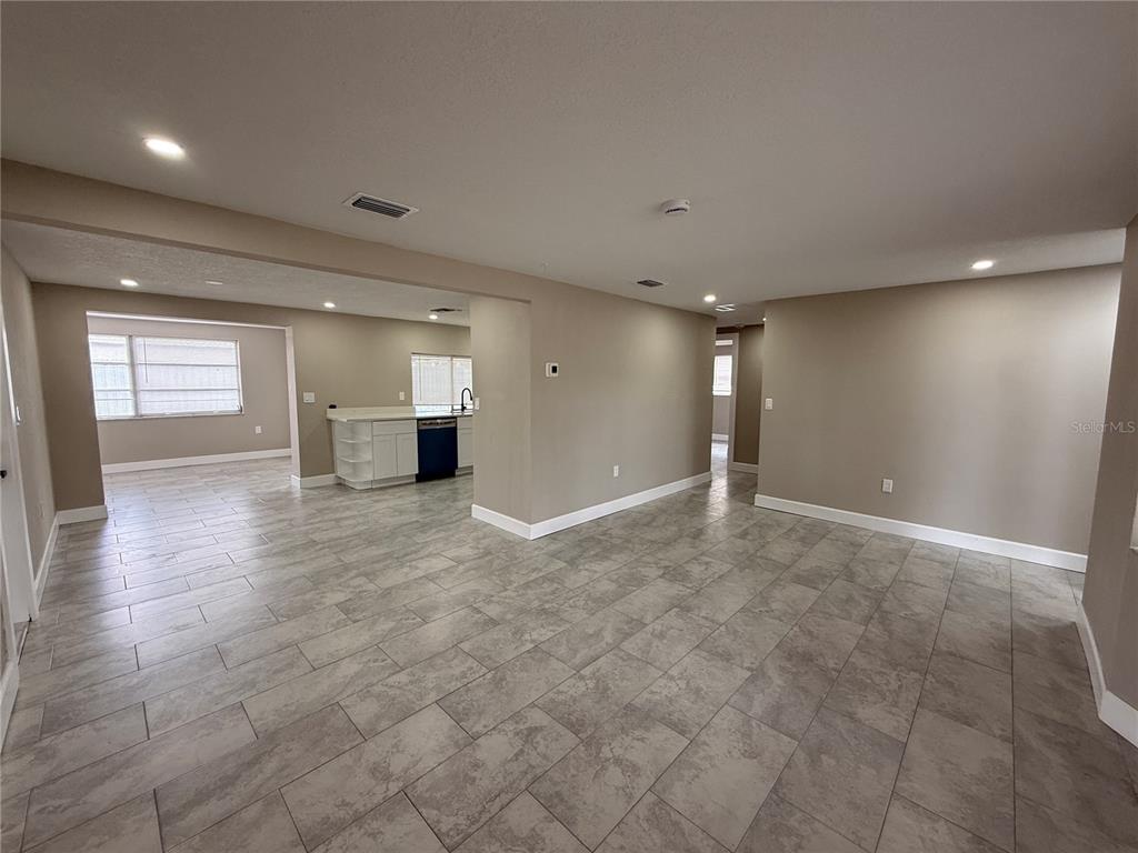 An open-concept living area features light wood-look flooring, a white kitchen, and sliding glass doors — 3019 LLOYD DRIVE, HOLIDAY, FL