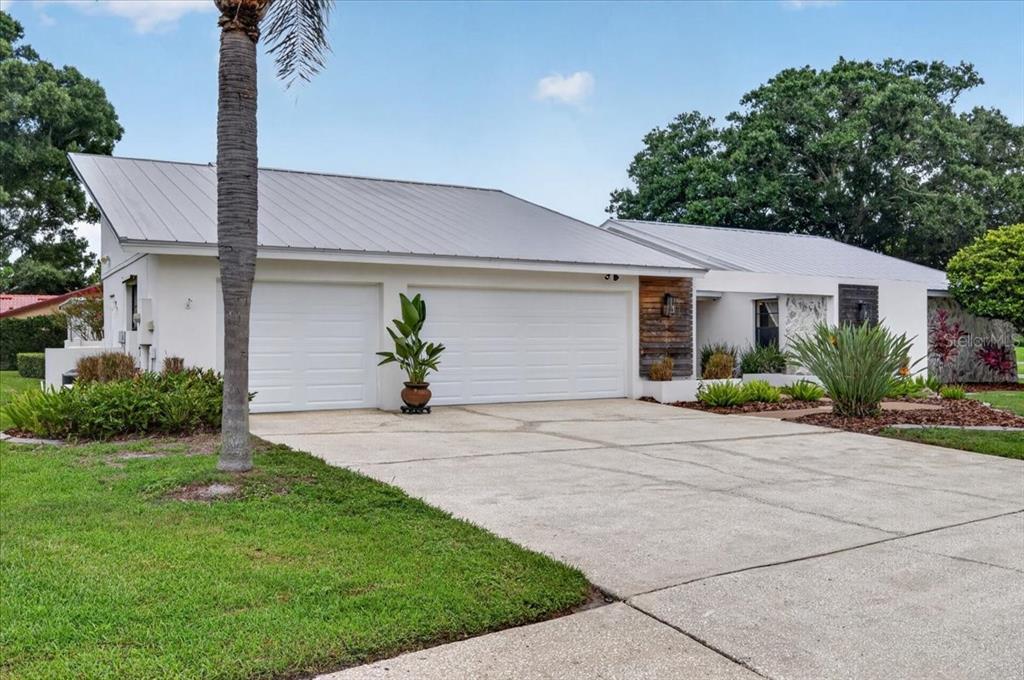 A white house with a metal roof, a three-car garage, and a concrete driveway — 2862 SHADY OAK COURT, CLEARWATER, FL