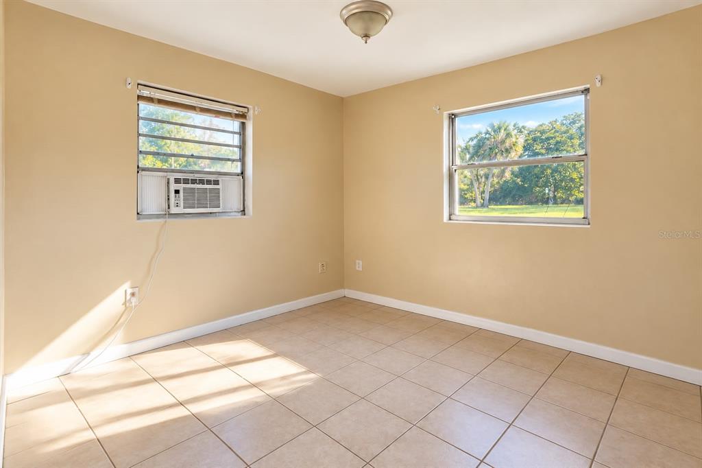 An empty room features beige walls, tiled flooring, two windows, and a ceiling light fixture — 157 E NORTHSIDE DRIVE UNIT 1, LAKE WALES, FL