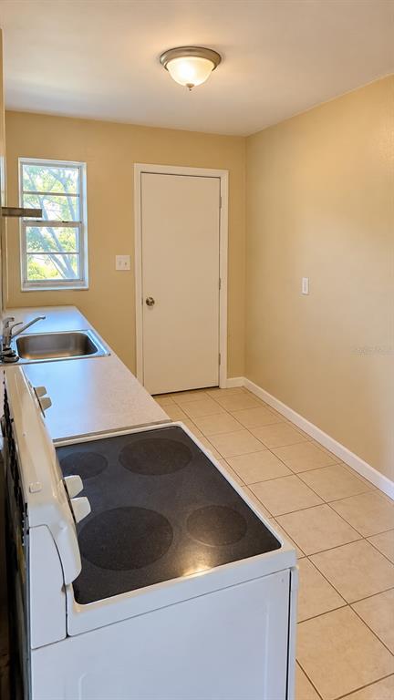 A kitchen features a white electric stove, a stainless steel sink, and beige tile flooring — 157 E NORTHSIDE DRIVE UNIT 1, LAKE WALES, FL