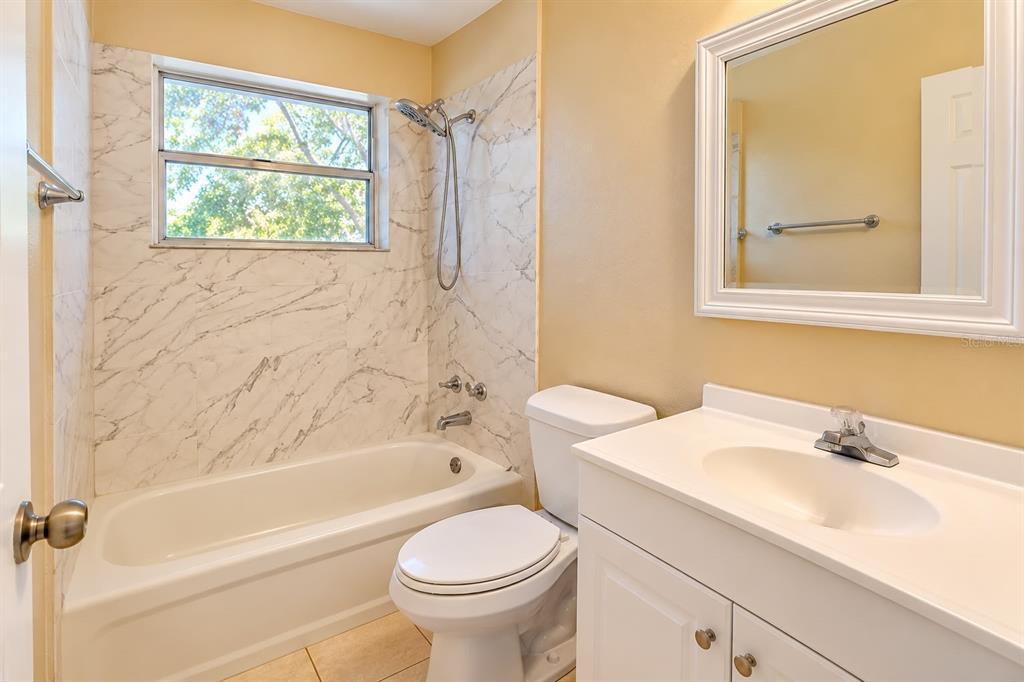 A bathroom features a white vanity, a toilet, and a bathtub with marble-patterned tile walls — 157 E NORTHSIDE DRIVE UNIT 1, LAKE WALES, FL