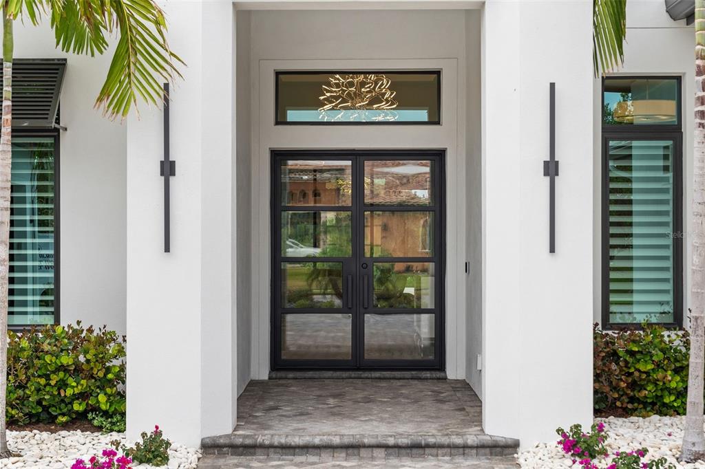 A modern white home entrance features black-framed double glass doors and two vertical wall sconces — 11721 RIVE ISLE RUN, PARRISH, FL