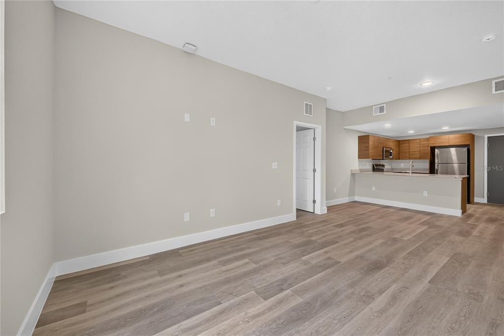 An open-concept living area features light gray walls, wood-look flooring, and an adjacent kitchen — 4424 S TEXAS AVENUE UNIT 217, ORLANDO, FL