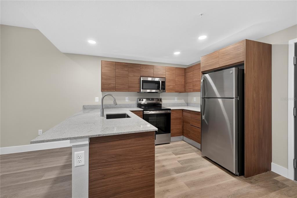 A modern kitchen features wood cabinets, stainless steel appliances, and a granite-topped island with sink — 4424 S TEXAS AVENUE UNIT 217, ORLANDO, FL