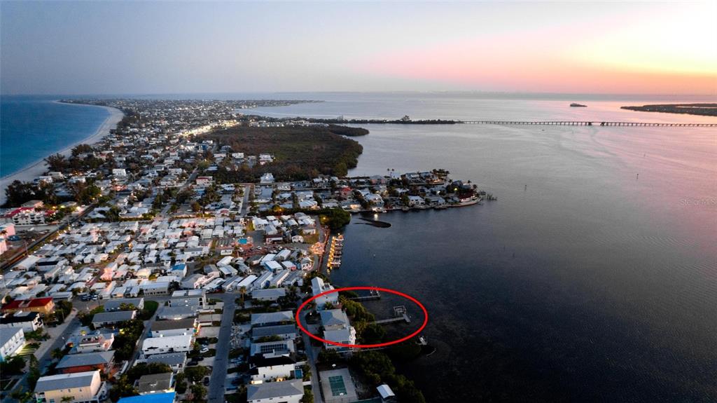 An aerial view shows a coastal neighborhood with a red circle highlighting a waterfront property — 2512 AVENUE A, BRADENTON BEACH, FL