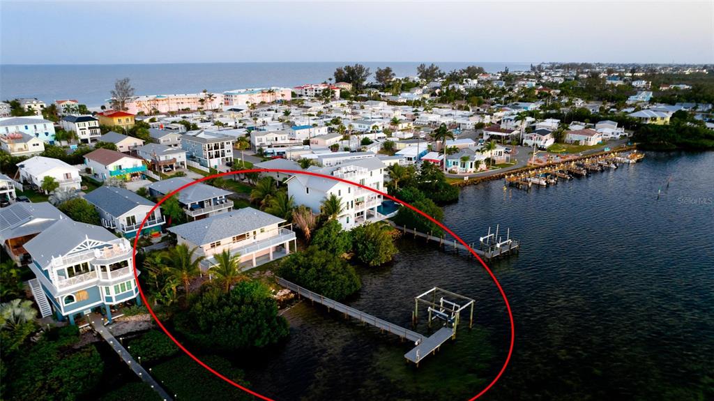 An aerial view shows a waterfront house with a private dock extending into the bay — 2512 AVENUE A, BRADENTON BEACH, FL