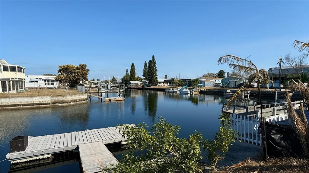 A canal view features a wooden dock in the foreground and residential homes beyond — 6411 TOWER DRIVE, HUDSON, FL