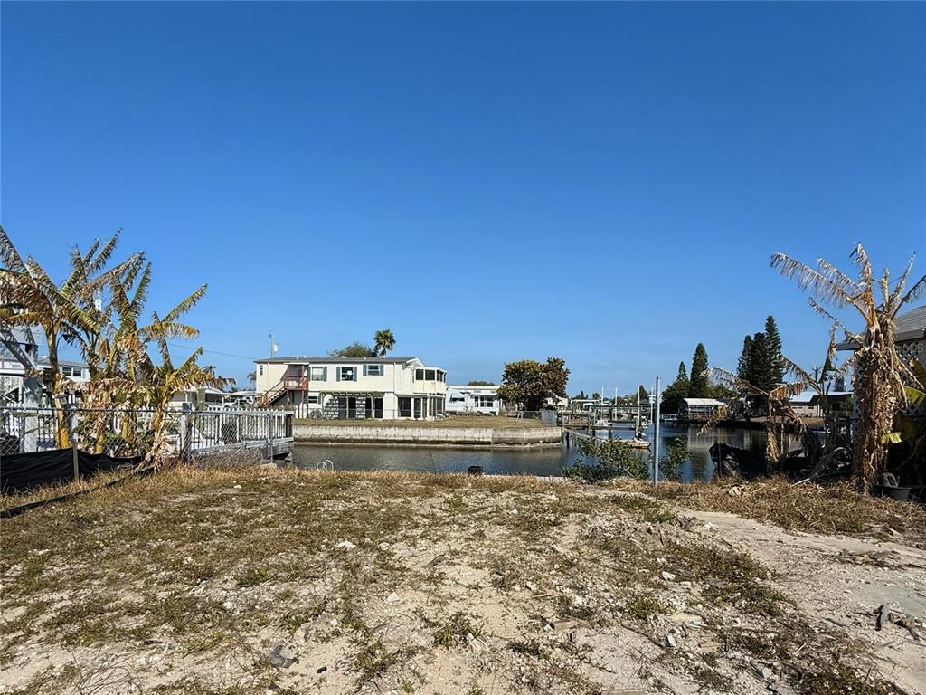 A vacant, sandy waterfront lot faces a canal with houses and boat docks across the water — 6411 TOWER DRIVE, HUDSON, FL
