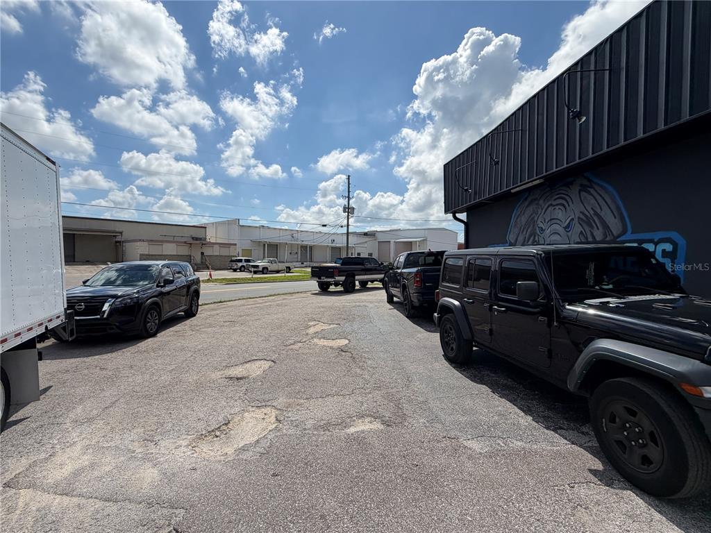An asphalt parking lot sits between a commercial building and a street with parked vehicles — 5983 49TH STREET N, ST PETERSBURG, FL