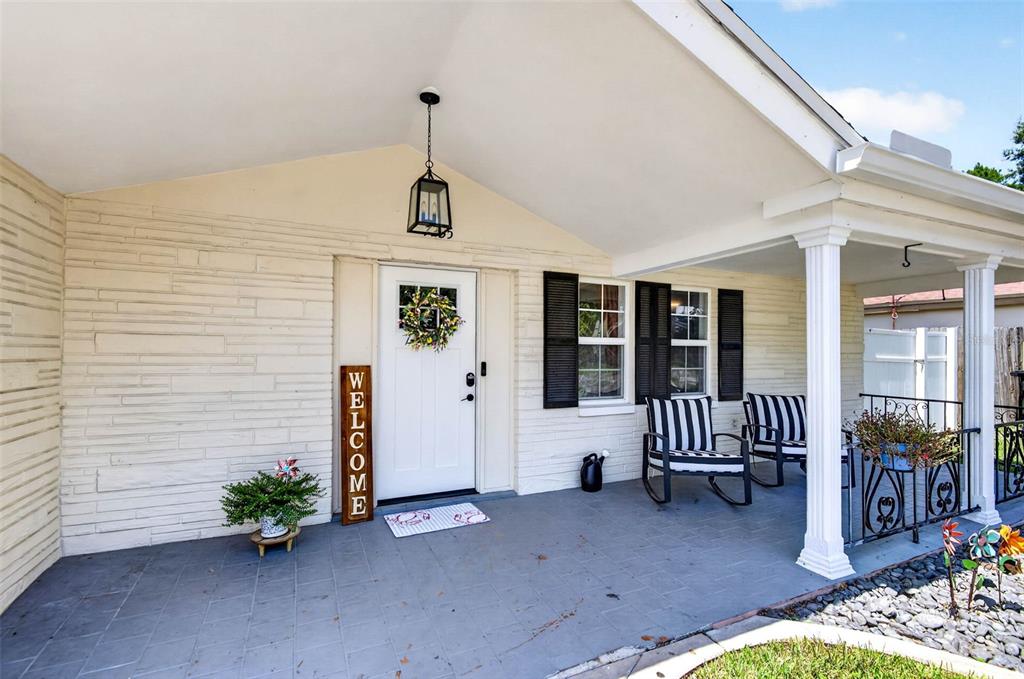 A covered front porch with a white door, rocking chairs, and stone-textured exterior walls — 7235 ASTOR DRIVE, NEW PORT RICHEY, FL