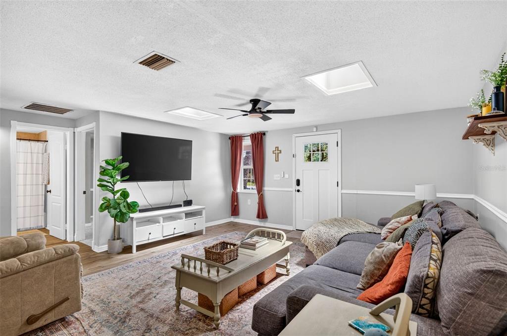 A living room features a gray sectional sofa, a television on a white stand, and skylights — 7235 ASTOR DRIVE, NEW PORT RICHEY, FL