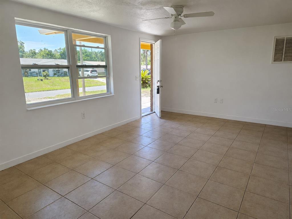 A room with beige tile flooring, a ceiling fan, and an open door to outside — 4645 IRENE LOOP, NEW PORT RICHEY, FL