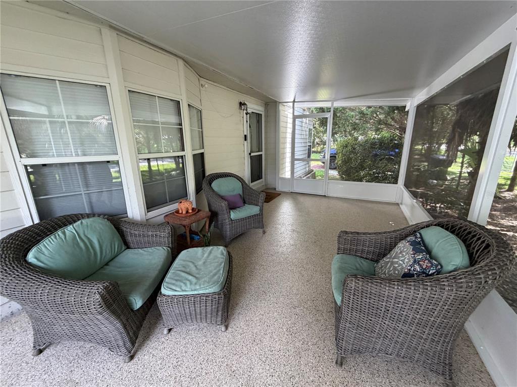 A screened-in porch features a wicker chair, speckled flooring, and views of palm trees — 421 MARGARET STREET, BRONSON, FL