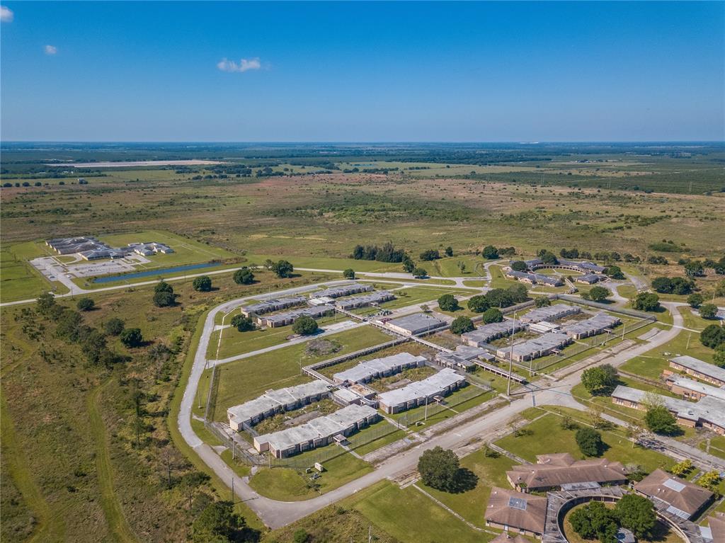 An aerial view shows a large complex of low-rise buildings surrounded by open grassy fields — 5871 SE HIGHWAY 31 UNIT 12, ARCADIA, FL