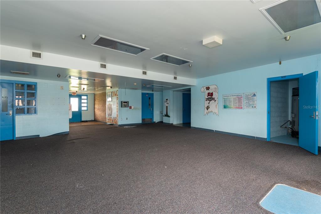 A large, empty room with light blue walls, dark carpeting, and several bright blue doors — 5871 SE HIGHWAY 31 UNIT 12, ARCADIA, FL