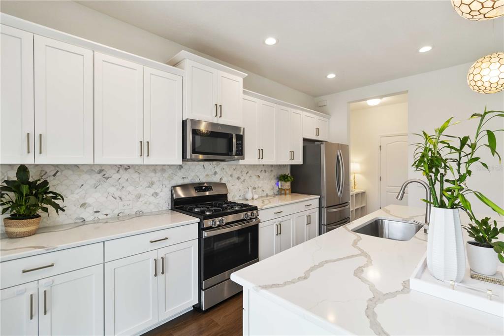 A modern kitchen features white cabinets, quartz countertops, a stainless steel stove, and a backsplash — 10109 CANAVERAL CIRCLE, SARASOTA, FL