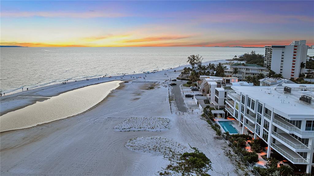 An aerial view shows a white sand beach, a tidal pool, and modern beachfront condominiums — 70 AVENIDA VENECCIA UNIT 202, SARASOTA, FL